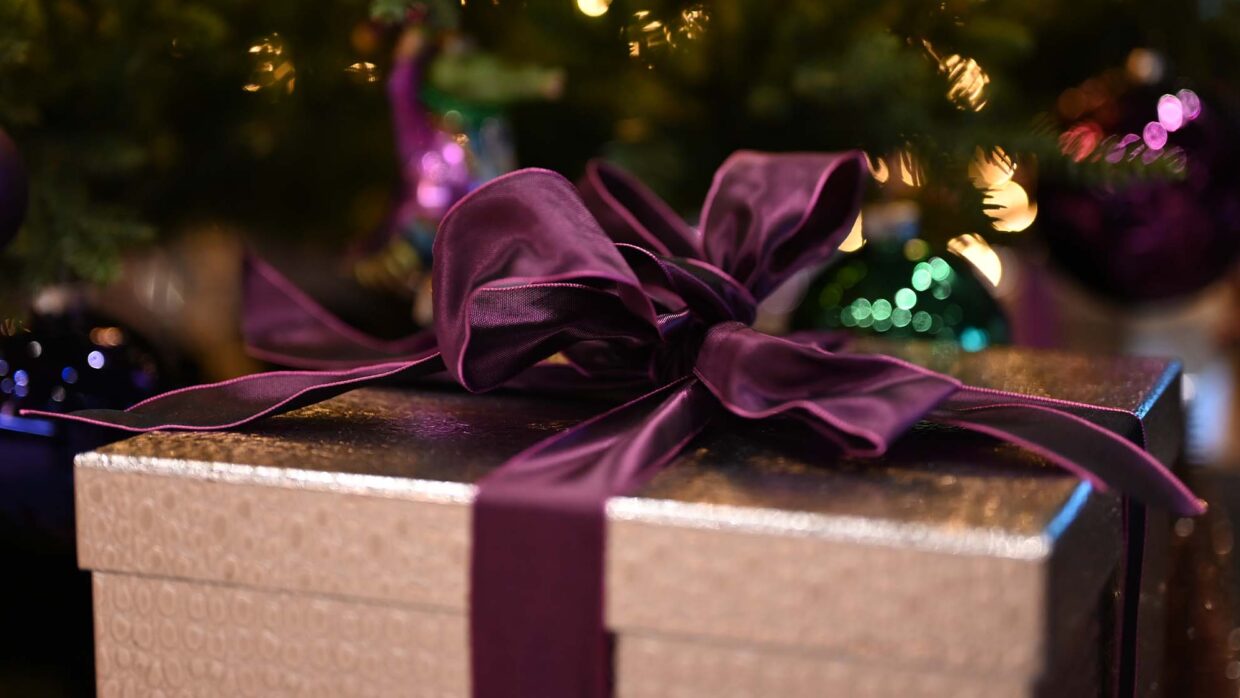 Weihnachtsgeschenk mit lila Schleife und Kugeln.