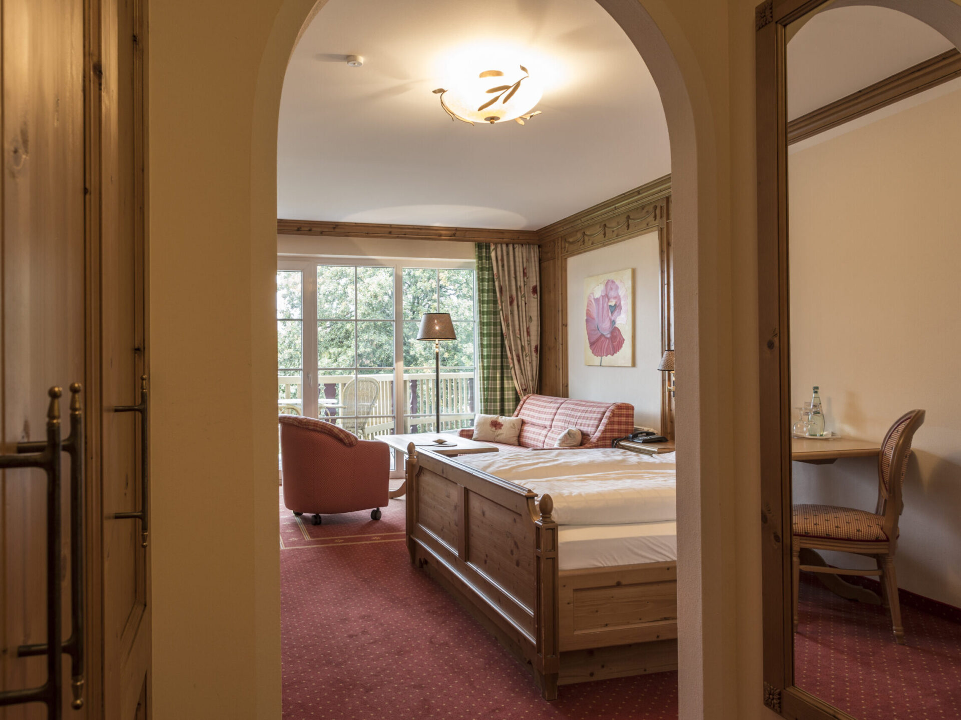 Room view of the Comfort room with country-style balcony through a round arch with a view of the bed, seating area and balcony at the Meiser SPA Resort