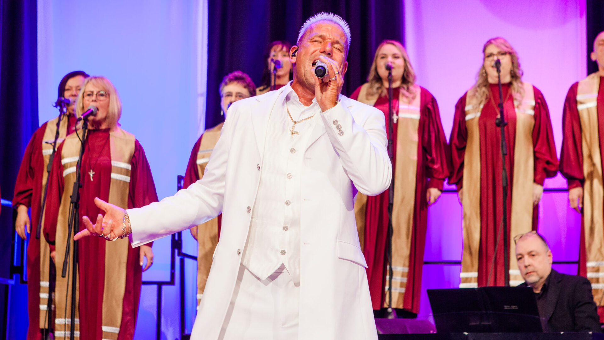 Mann in weißem Anzug singt vor Chor.