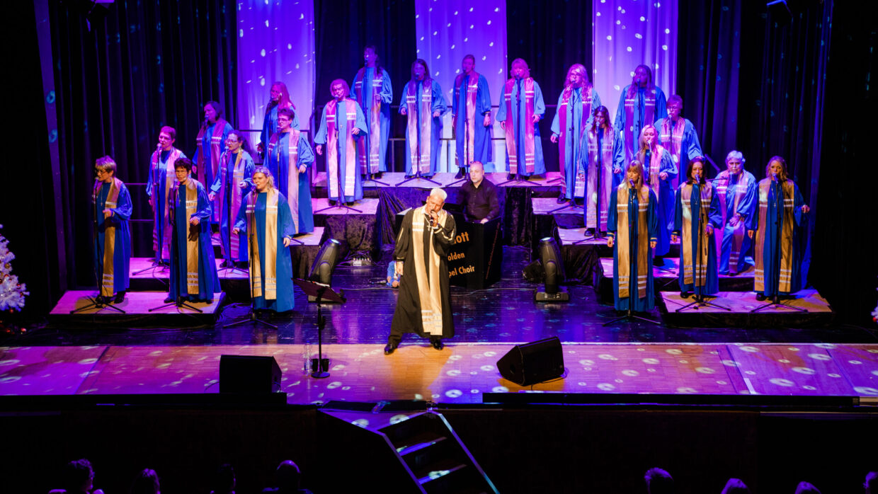 Gospelchor singt auf beleuchteter Bühne in blauen Roben.