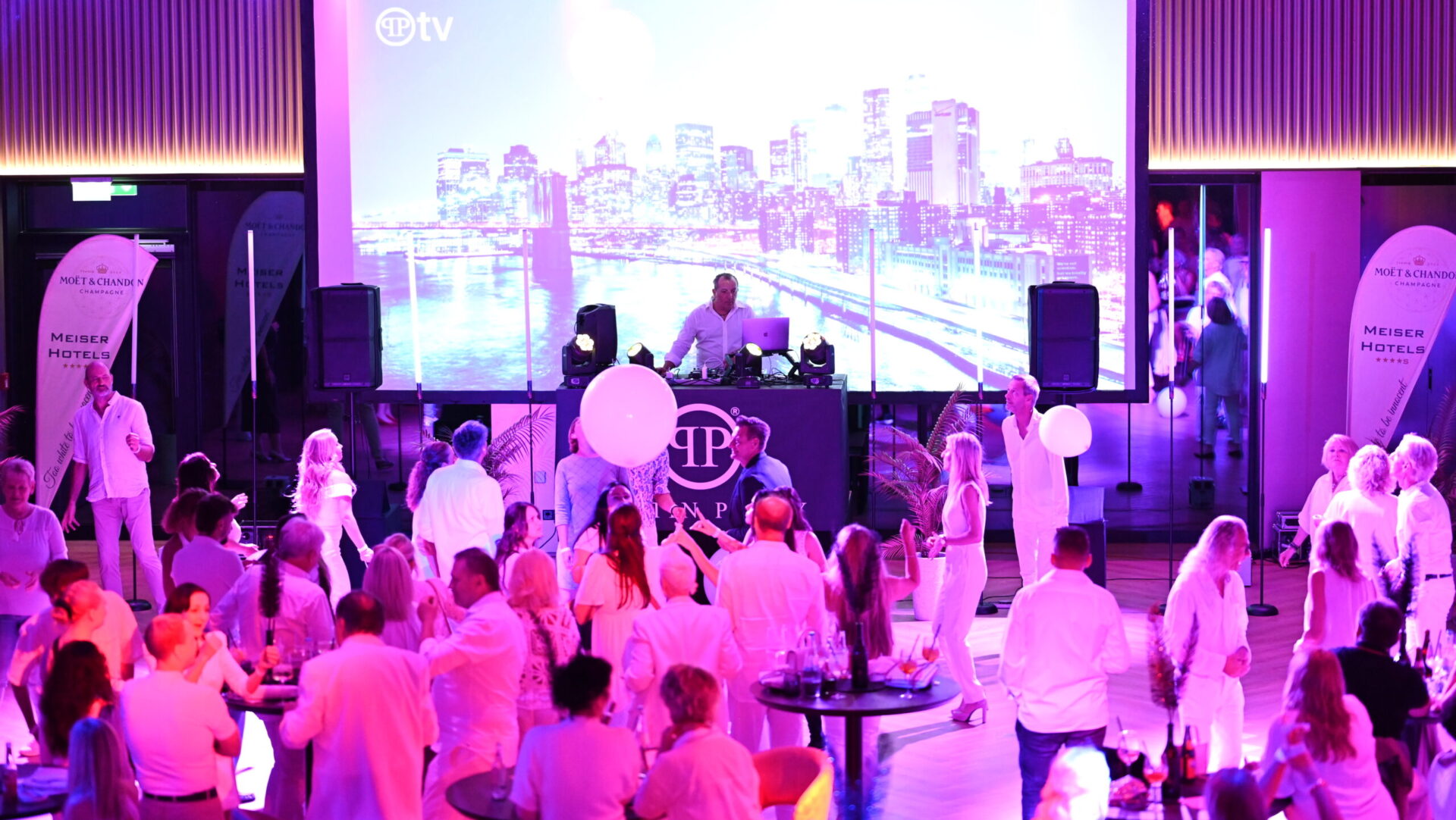 People dancing at a party with DJ and big screen.