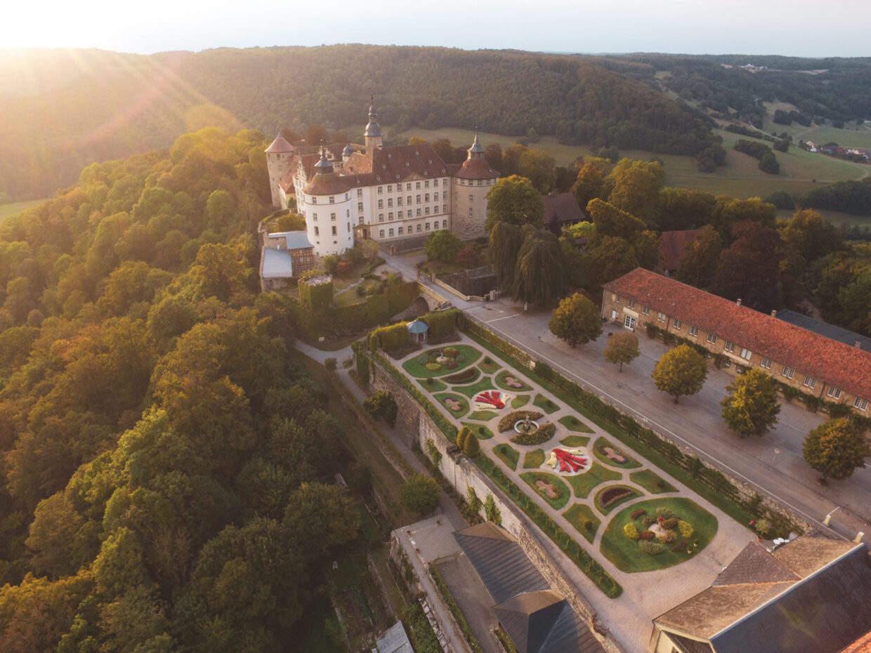 Luftaufnahme eines großen Schlosses umgeben von Wald.