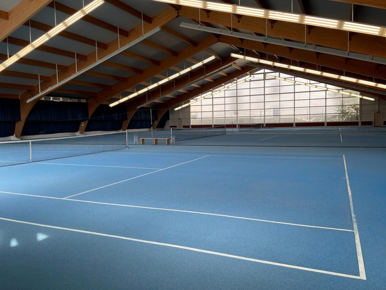 Leere Tennishalle mit blauen Spielfeldern.