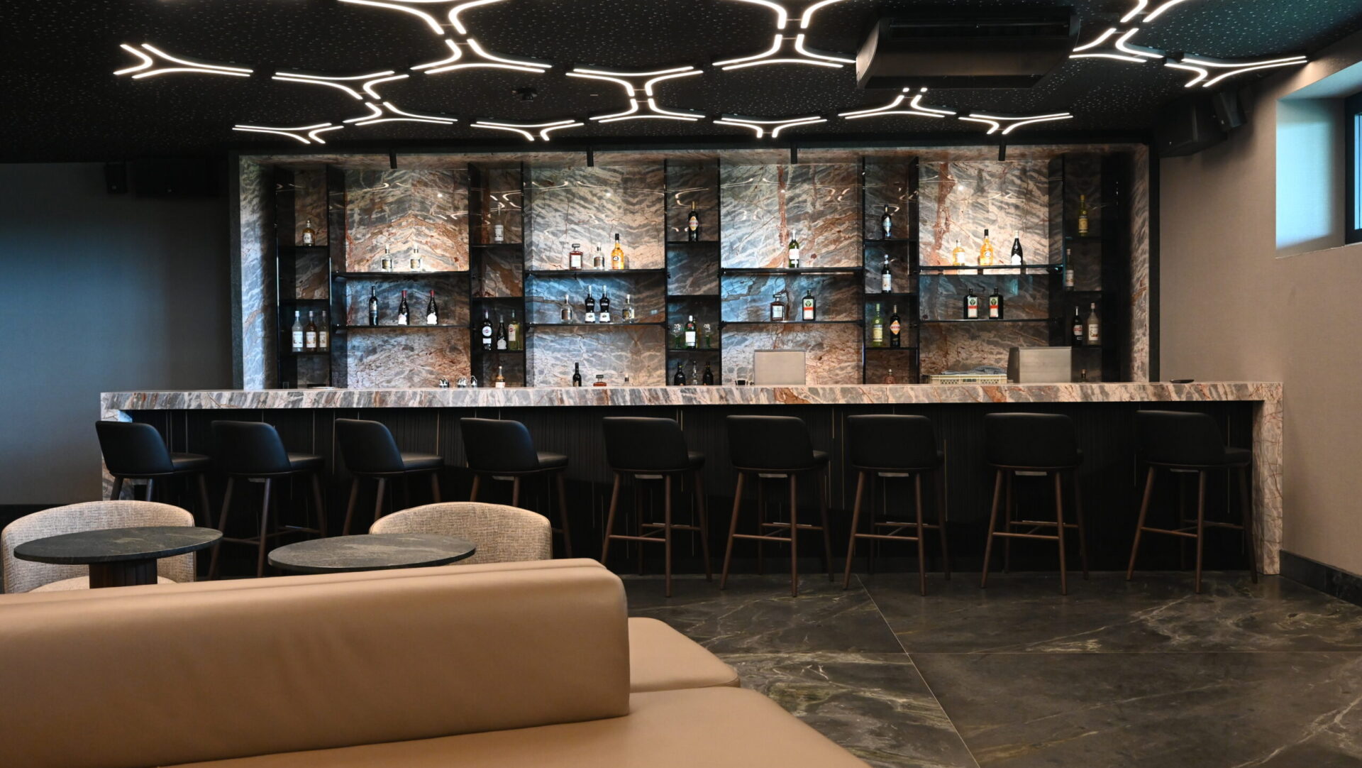 Elegante Bar mit Marmor, Flaschenregalen und geschwungenen Deckenleuchten