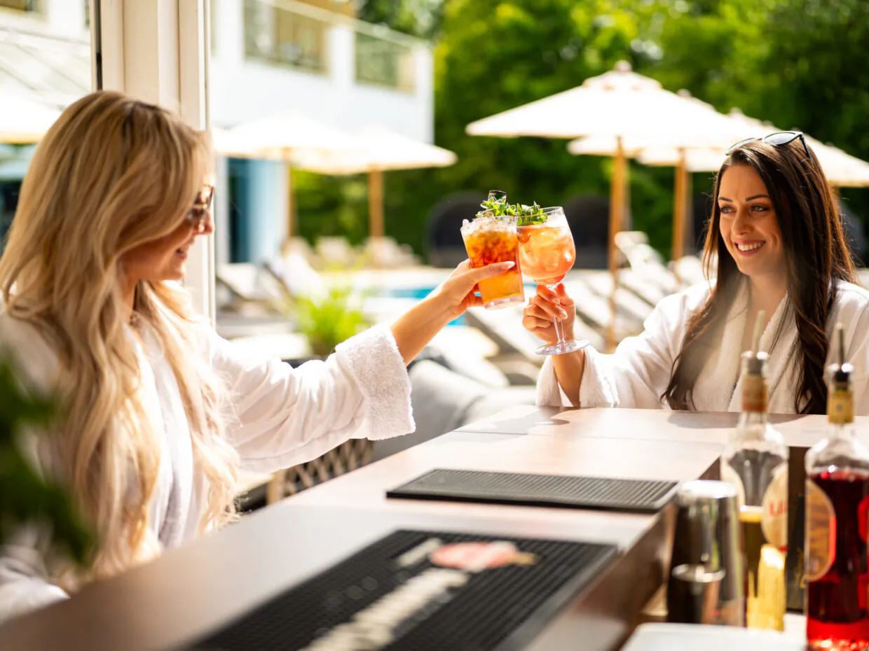 Frauen prosten mit Cocktails an Poolbar.