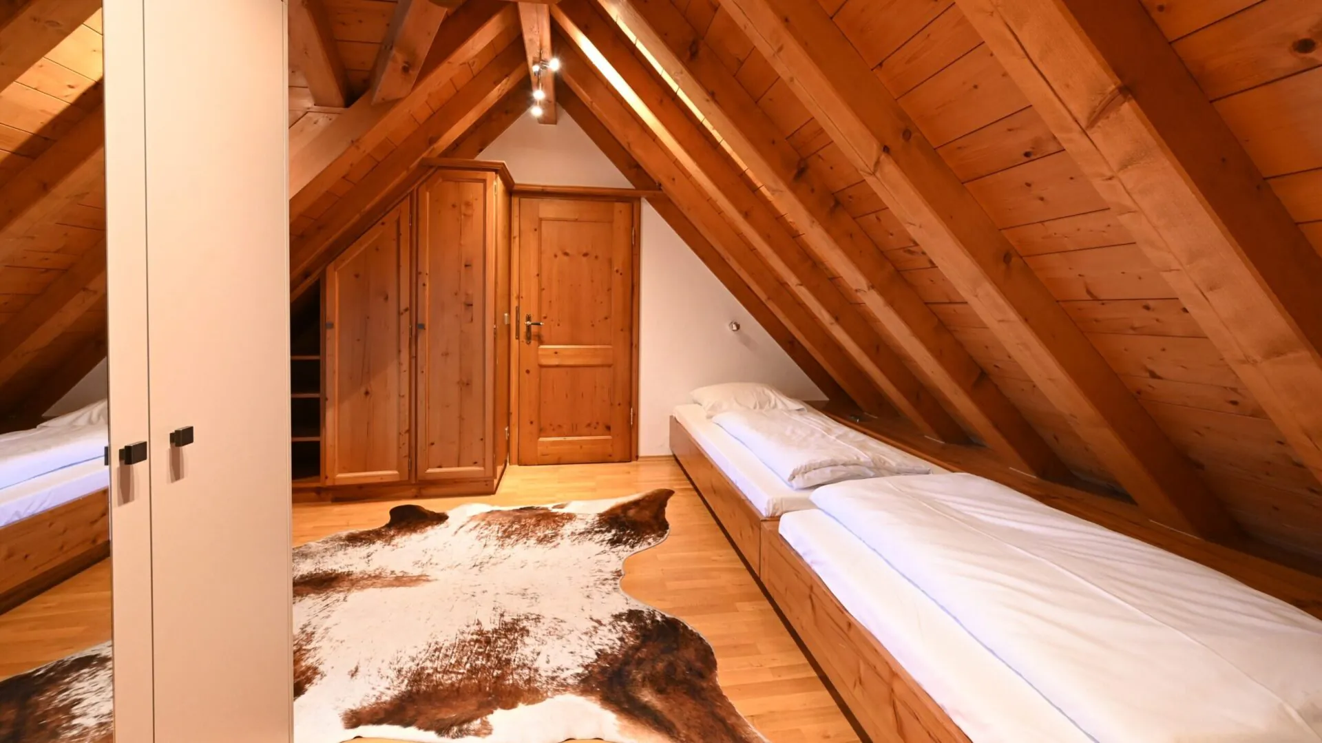 Gemütliches Dachzimmer mit Holzmöbeln und Tierfell-Teppich.