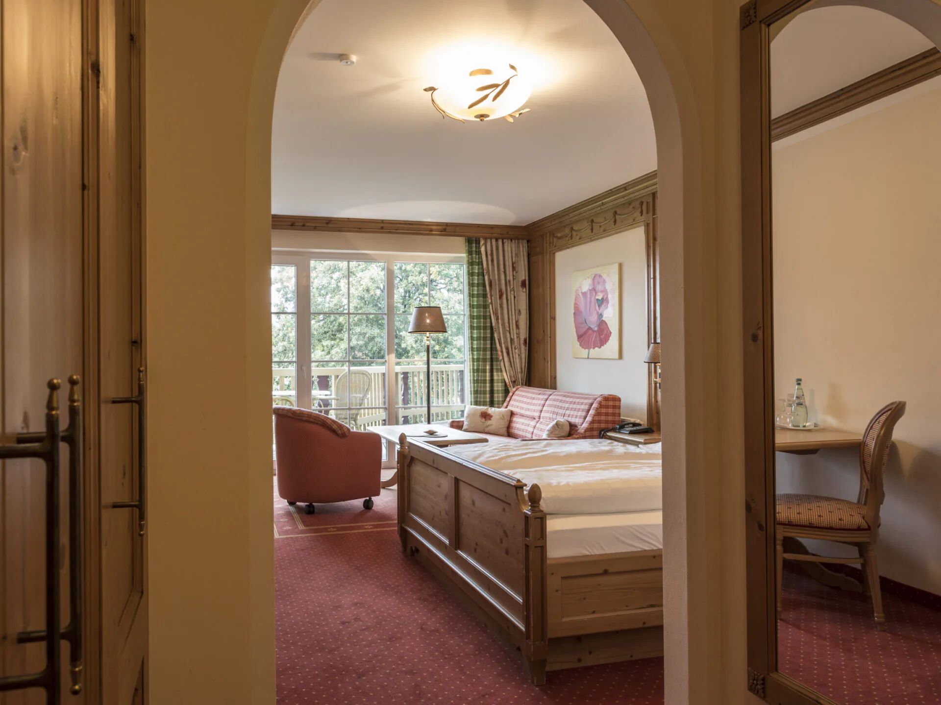 Zimmeransicht des Comfort Zimmer mit Balkon im Landhausstildurch einen Rundbogen mit Blick auf Bett, Sitzgruppe und Balkon im Meiser SPA Resort