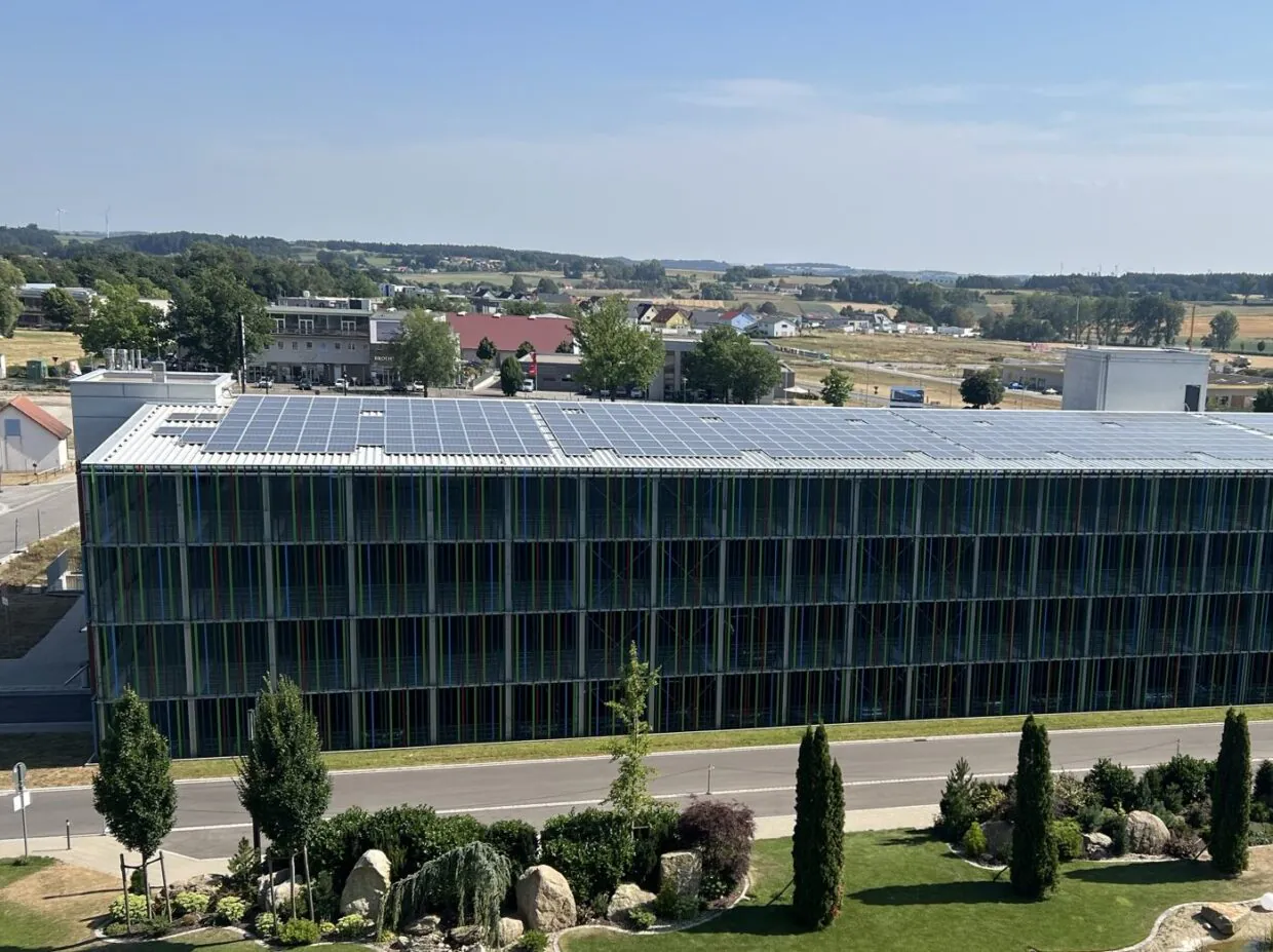 Gebäude mit Solarmodulen und Landschaft im Hintergrund.