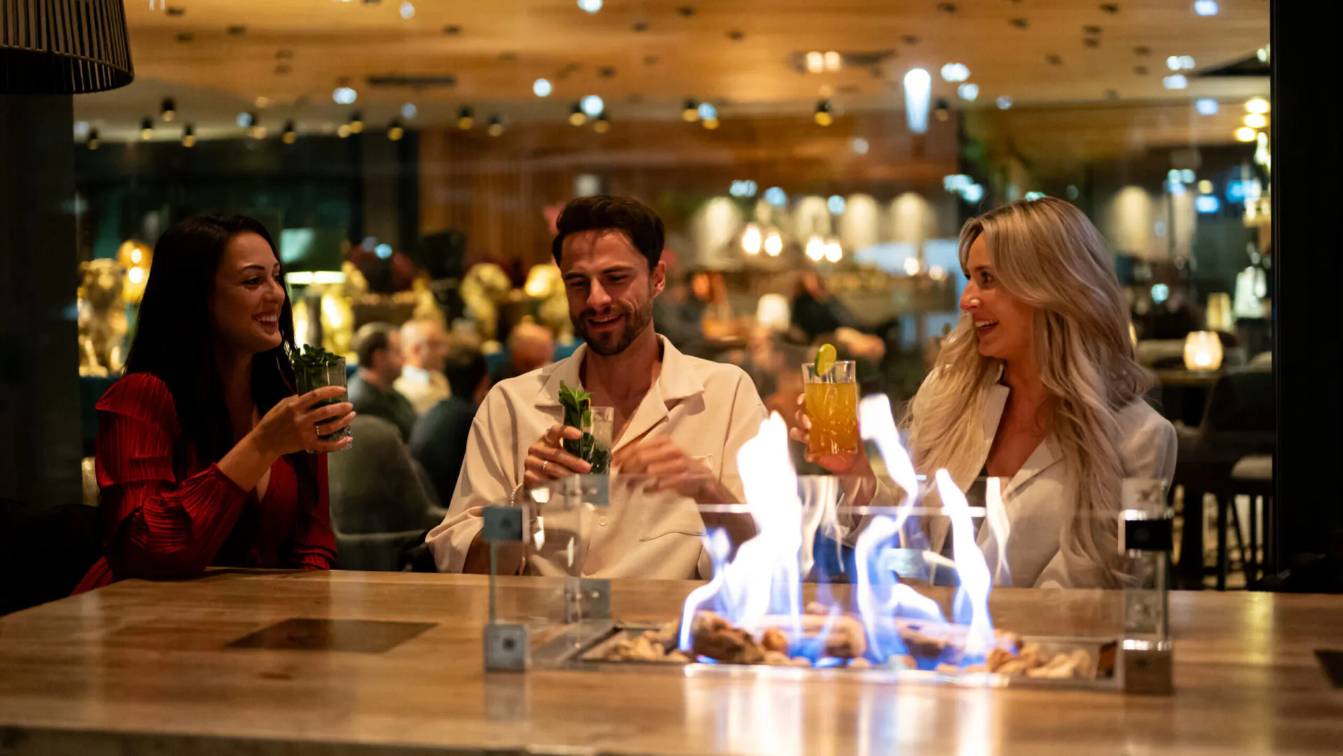 Leute trinken Cocktails an einem Tisch mit Feuer.