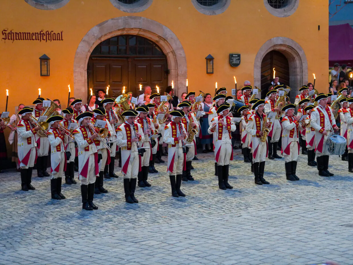 Marschkapelle in historischen Uniformen vor gelbem Gebäude.