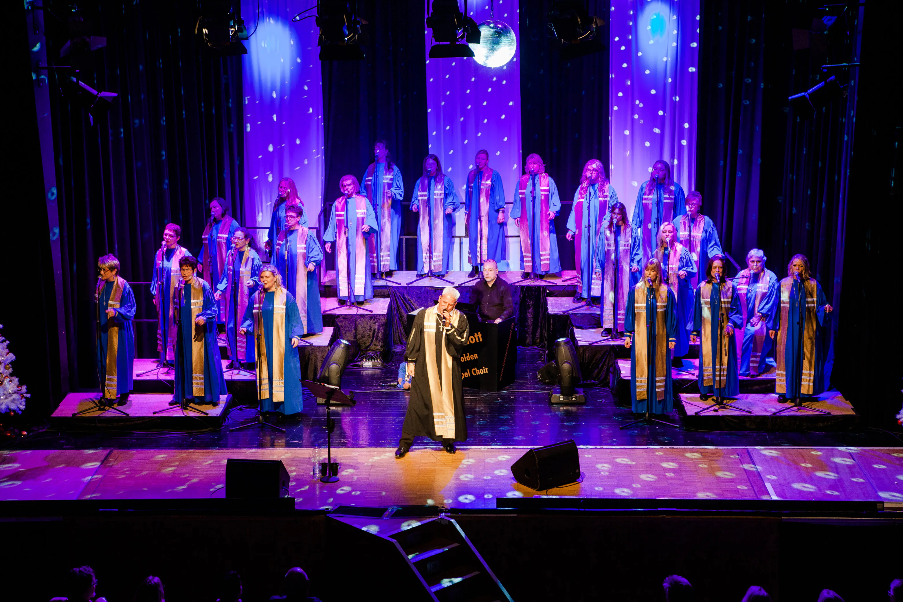 Gospelchor singt auf beleuchteter Bühne in blauen Roben.