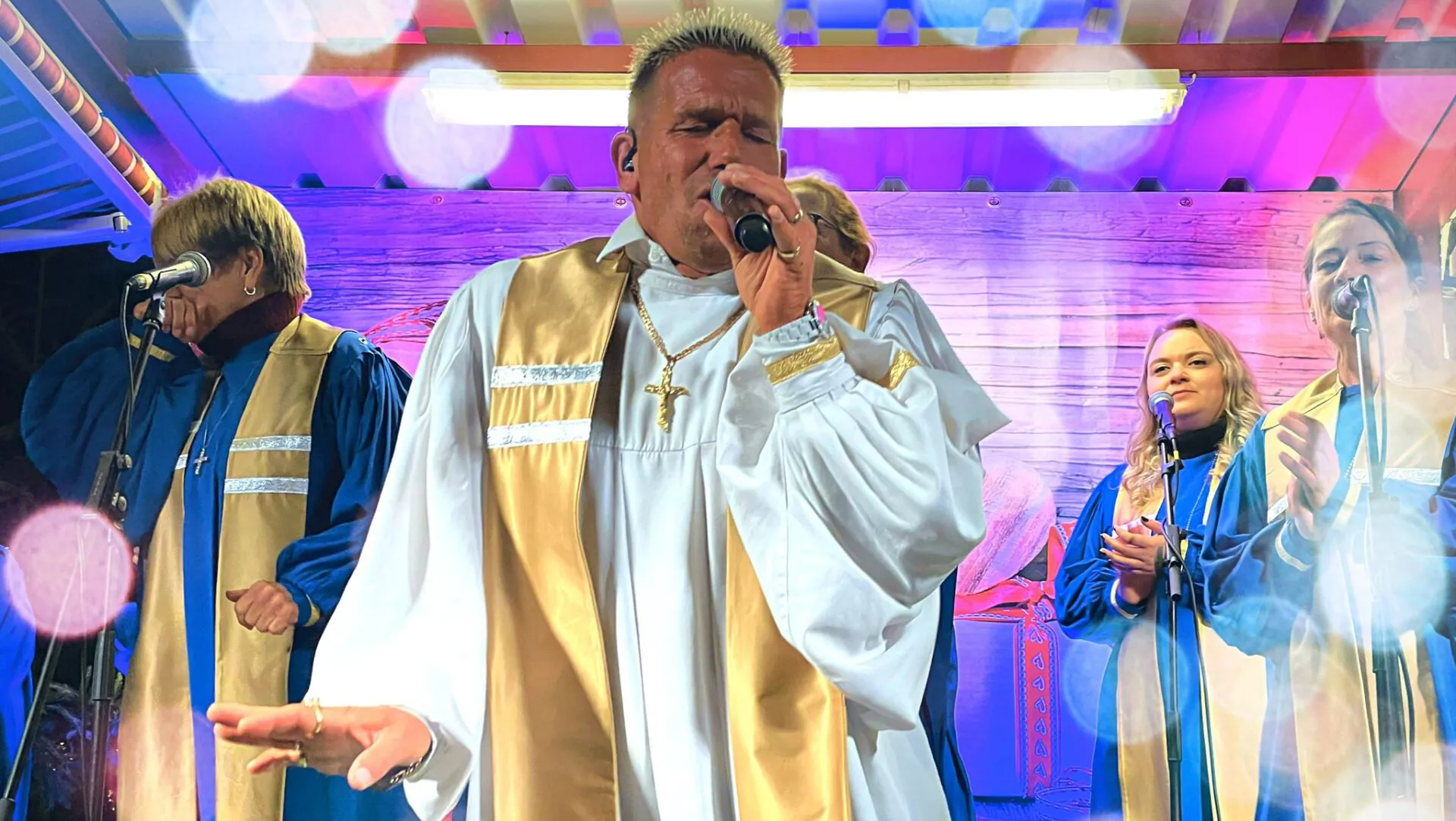 Gospelchor mit Sänger im weißen Gewand auf Bühne.