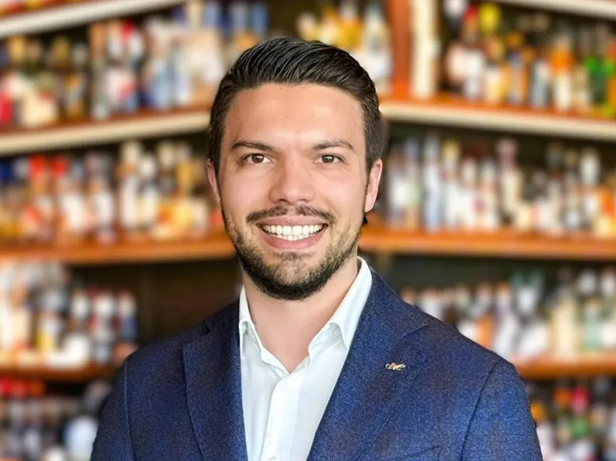 Lächelnder Mann im Anzug vor unscharfem Hintergrund.