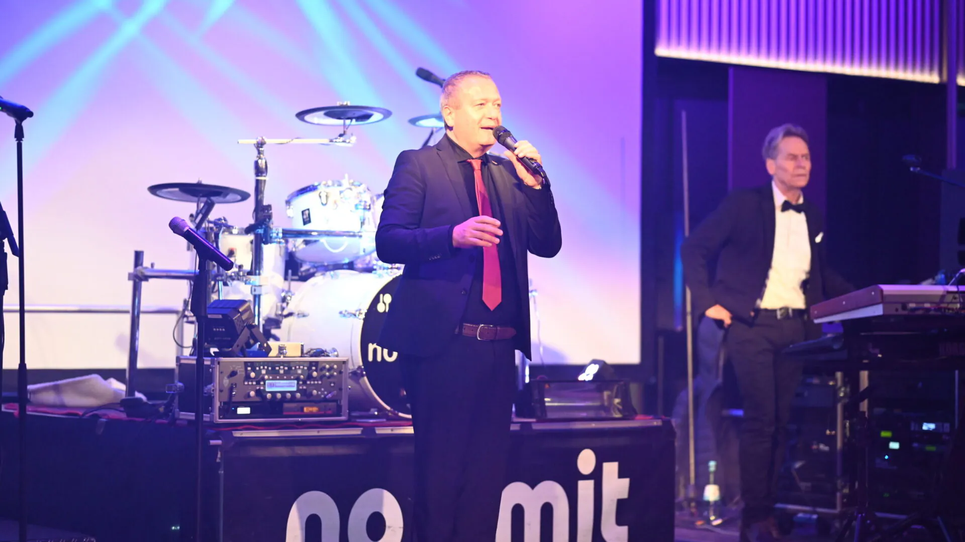 Armin Meiser redet auf Bühne mit Schlagzeug im Hintergrund im Meiser Congress Plaza.