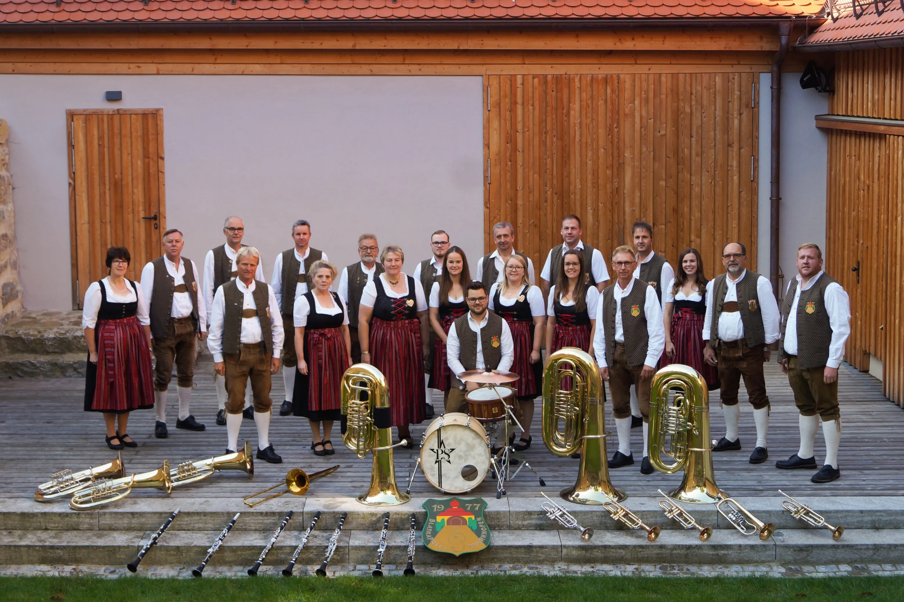 Blaskapelle in Trachten mit Instrumenten vor Holzwand.